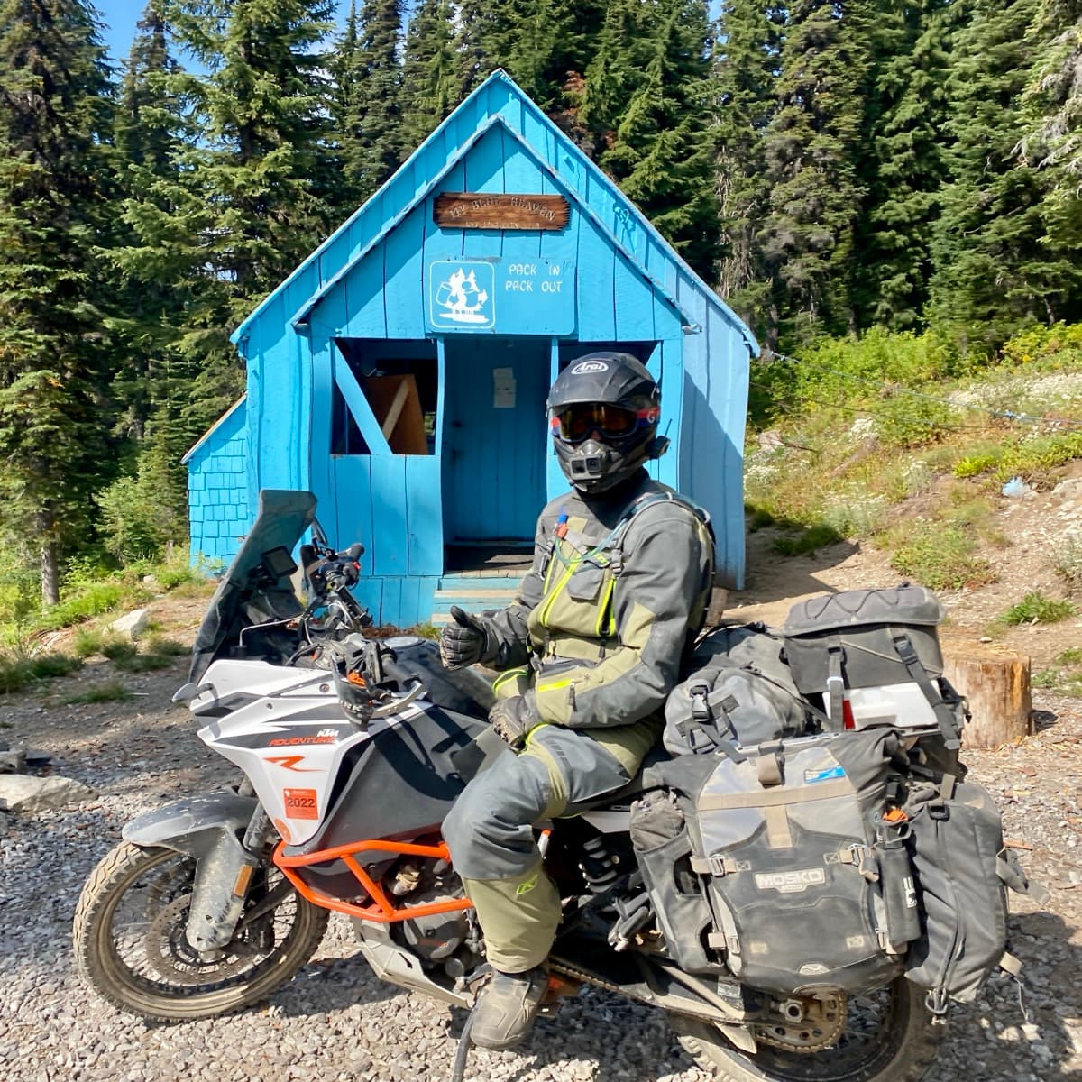 Rider on a KTM Adventure motorcycle with Mosko Moto bags in front of a blue mountain cabin